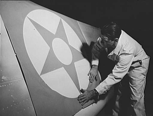 Рабочий кузовостроительного предприятия Briggs Manufacturing Company наклеивает знаки отличия на крыло бомбардировщика